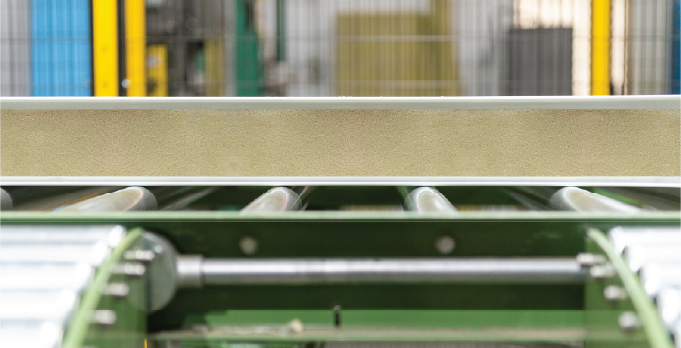 Close-up of an insulated panel moving along rollers during production.