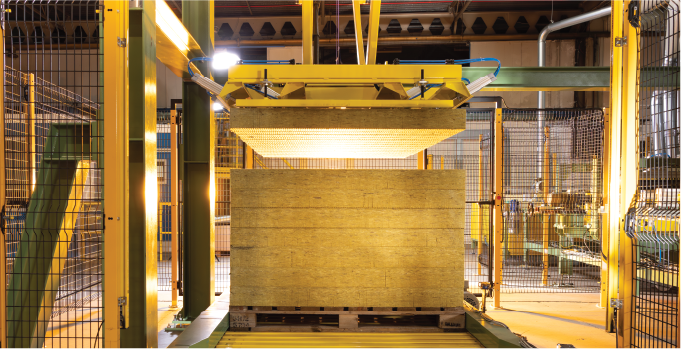 Stacked mineral wool core being processed using automated factory equipment.