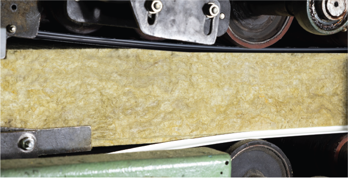 Close-up of mineral wool core passing through production rollers.
